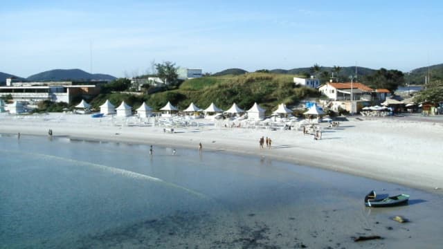 Praia de areia branca em Cabo Frio com quiosques brancos, banhistas e barcos à beira-mar